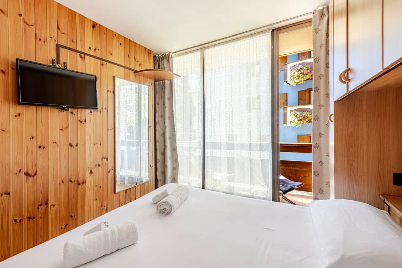 Schlafzimmer mit weißem Bett und Holzwänden, in Bormio