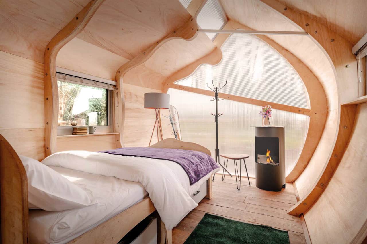 Monocoque Cabin — The bed sits within the curved plywood structure, with a biofuel fire alongside for the evenings.