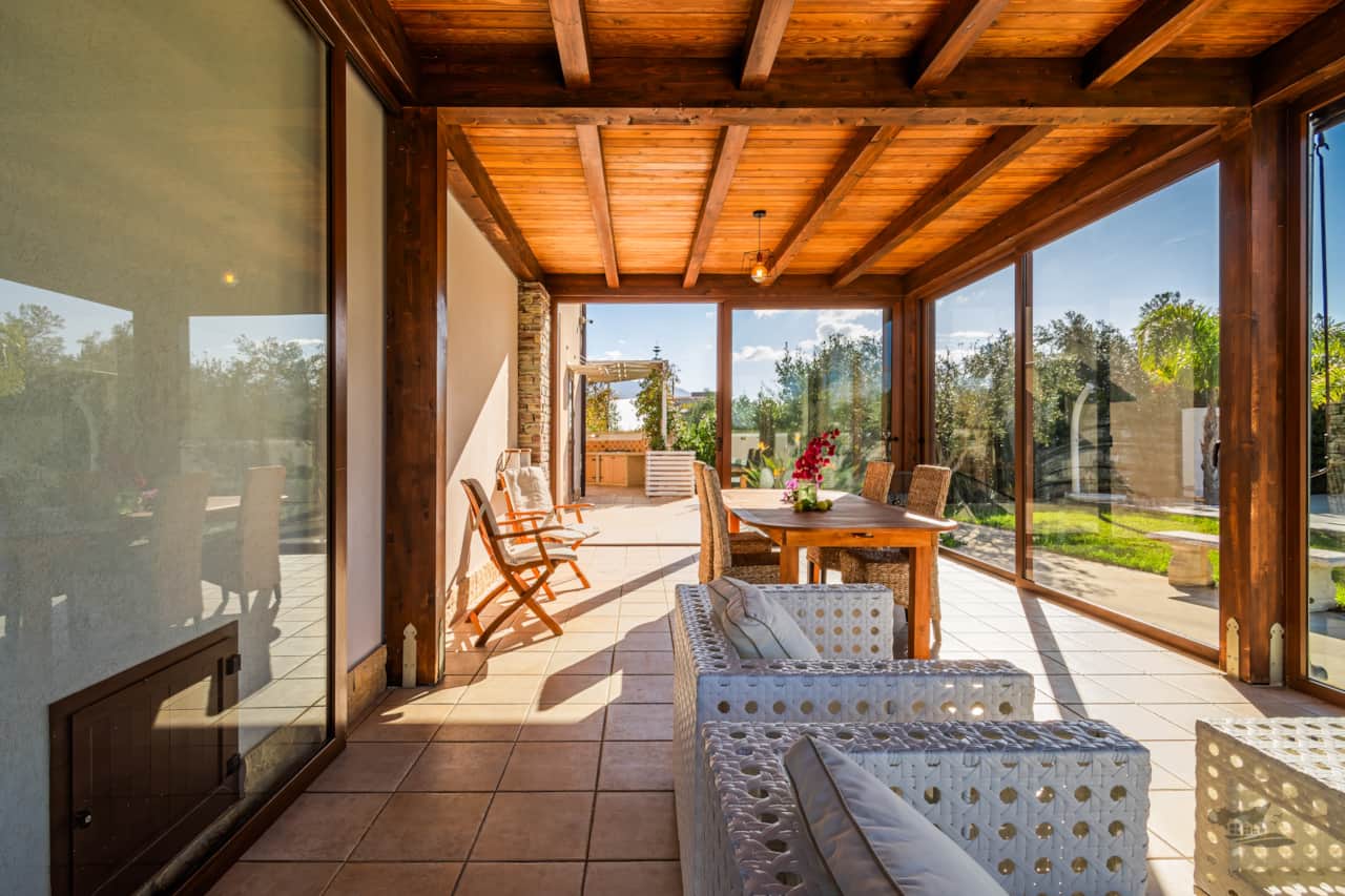 Sunlit veranda with dining table, lounge seating, and wide glass doors to the garden.