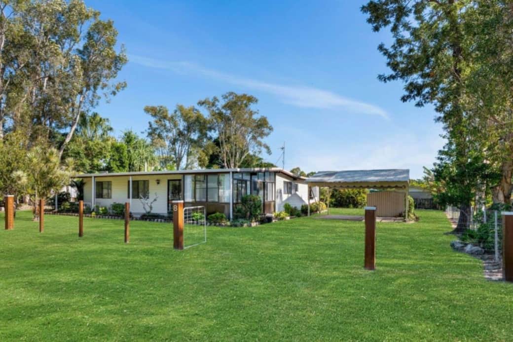 Street-facing view of the property showcasing the large, fully fenced yard. Features include a carport and a sunroom positioned on the front corner.