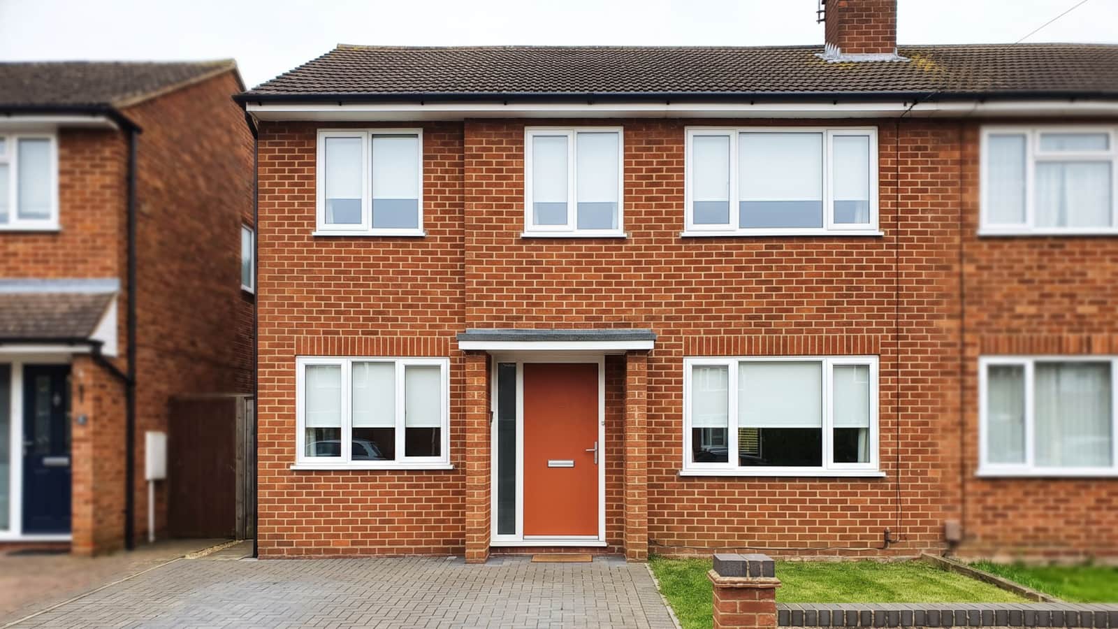 An empty two-storey red-brick semi-detached house with a burnt orange front door