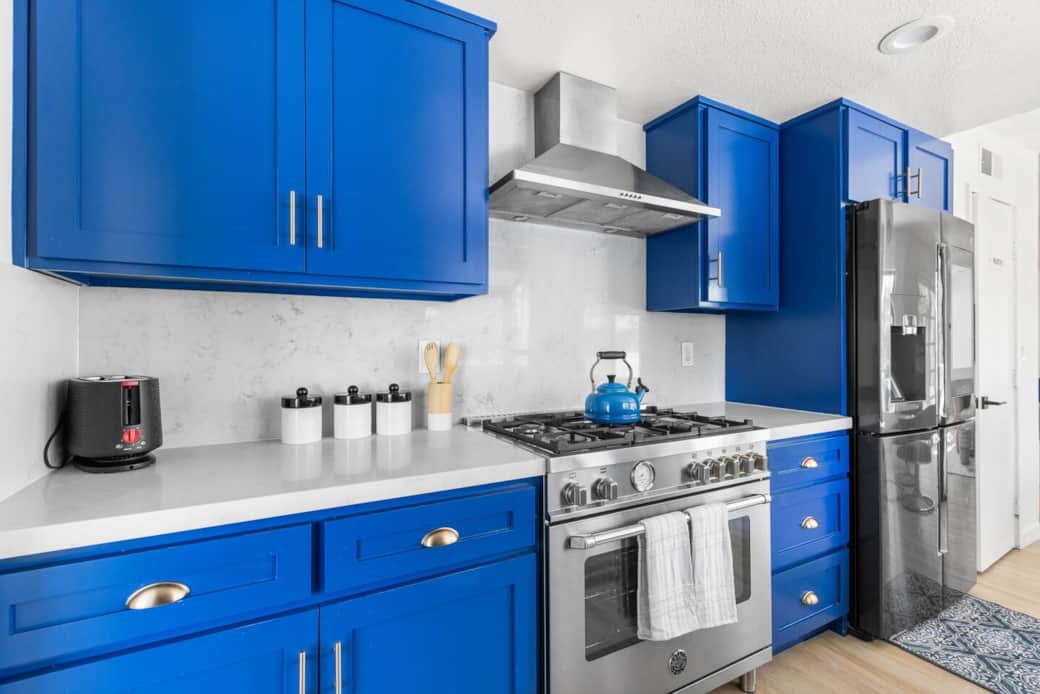 Modern gas range and blue cabinets with a white backsplash for a fresh stainless steel style.