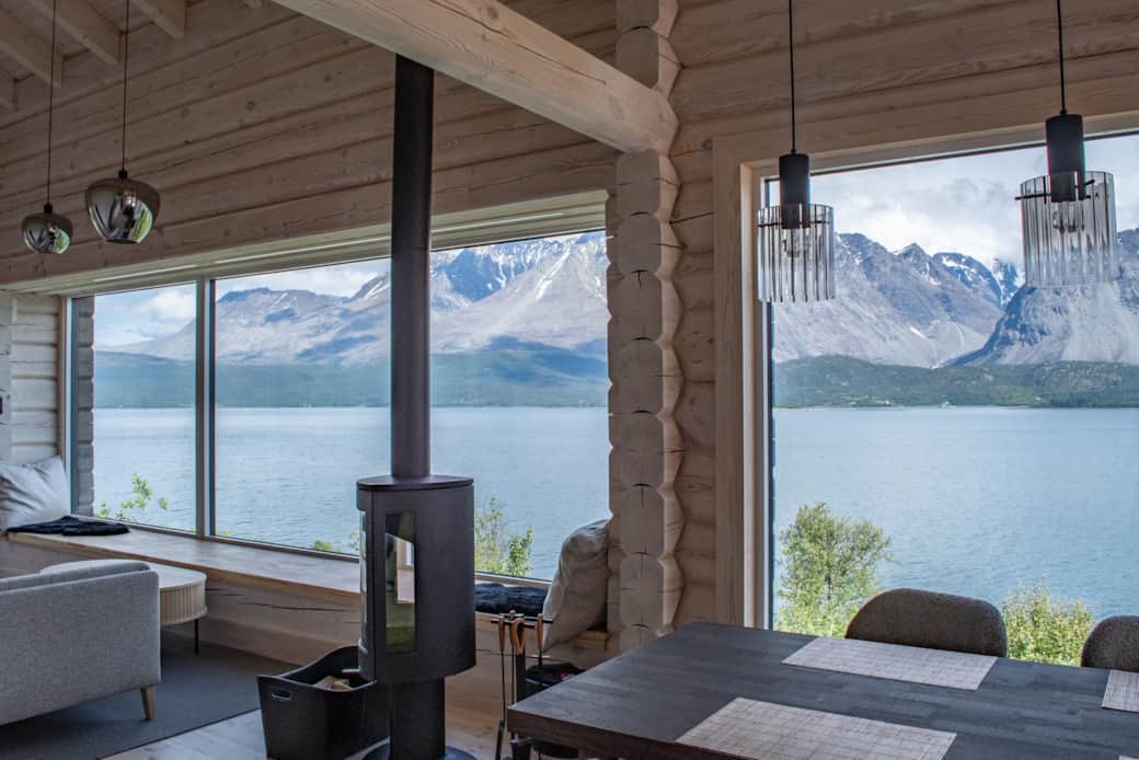 A wood stove between timber walls and the mountains beyond the glass.