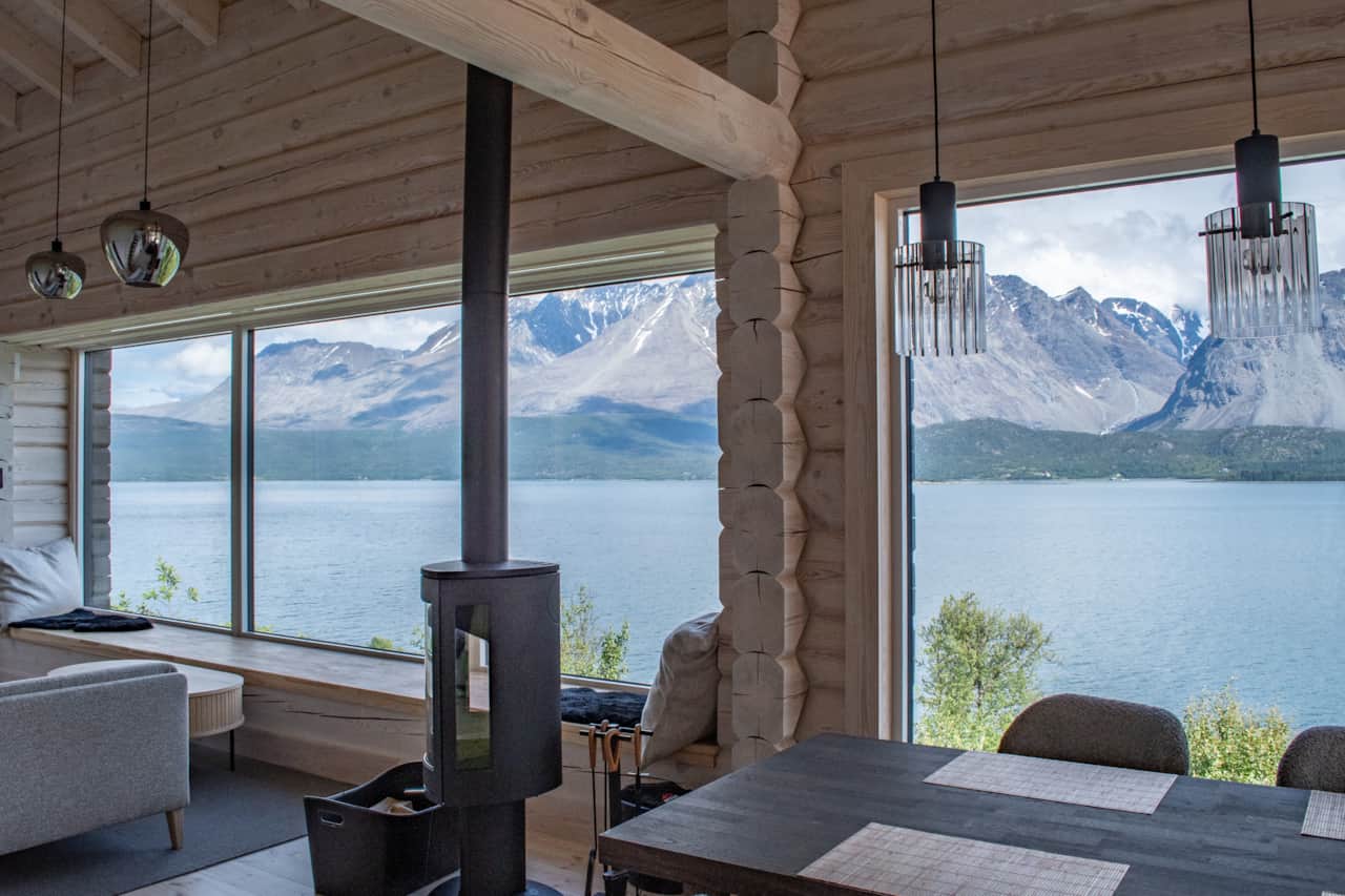 A wood stove between timber walls and the mountains beyond the glass.