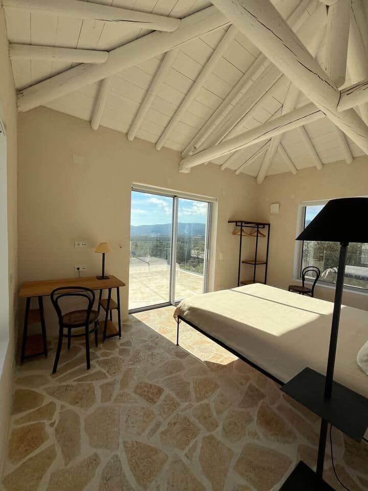 Bathed in natural light, this serene bedroom blends whitewashed beams, stone floors, and soft textiles. The high ceiling creates a sense of space and calm, inviting deep rest, slow mornings, and the quiet luxury of Mediterranean living.