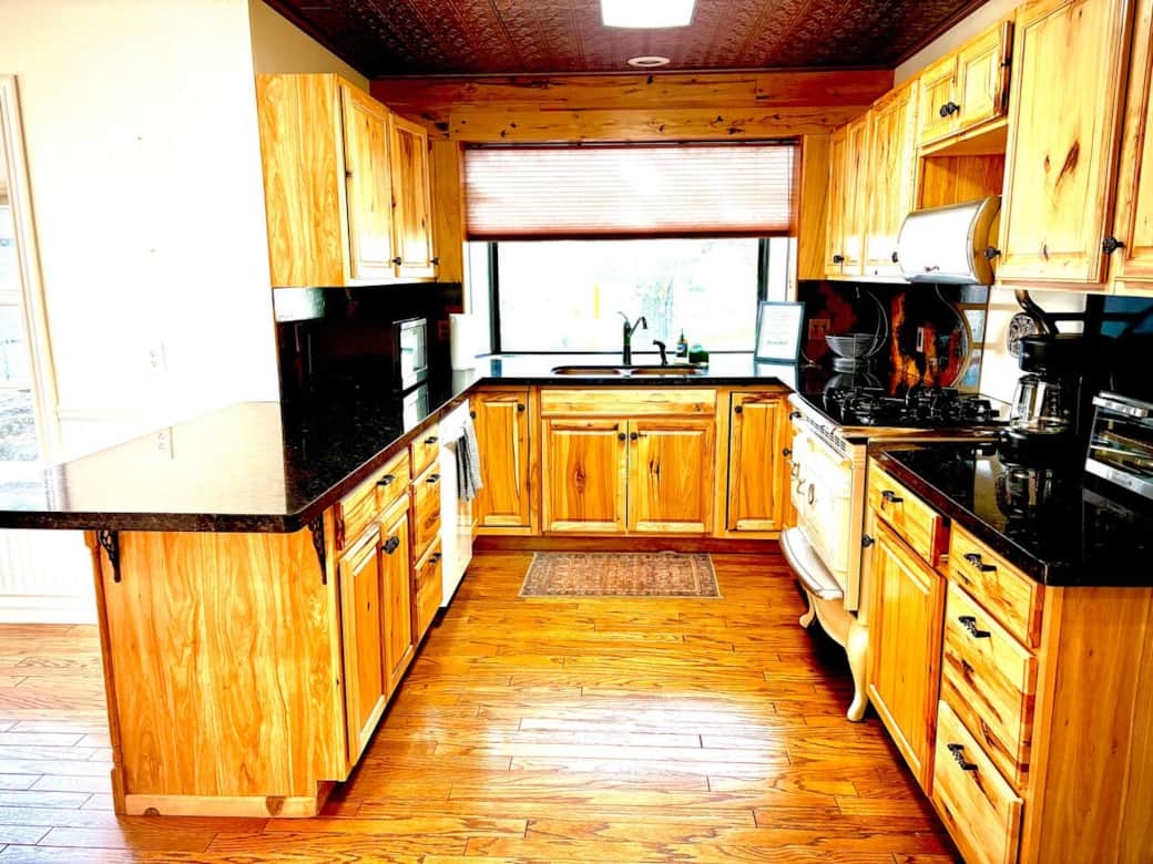 Charming kitchen with rustic cabinets. Features copper tin ceiling, modern appliances, and granite countertops. Hardwood floors and natural light in a well-equipped cooking space.
