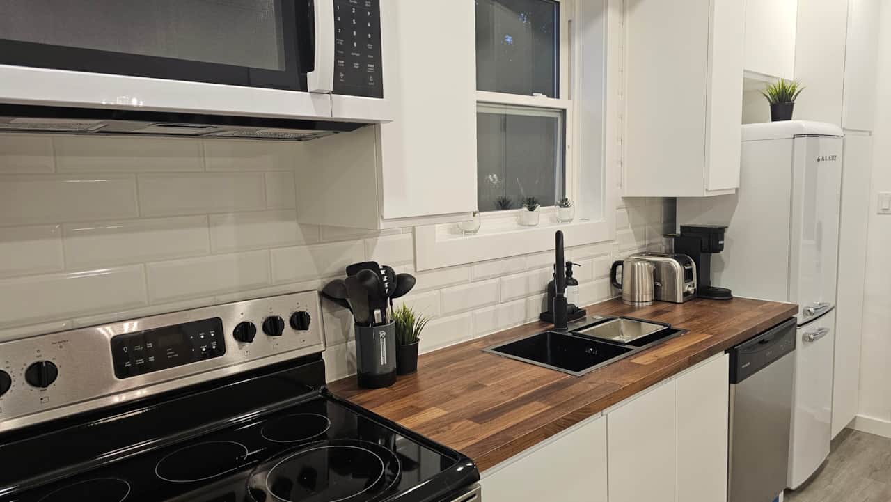 Updated kitchen with full-size stove, white cabinetry, wood countertops, and modern finishes in a do