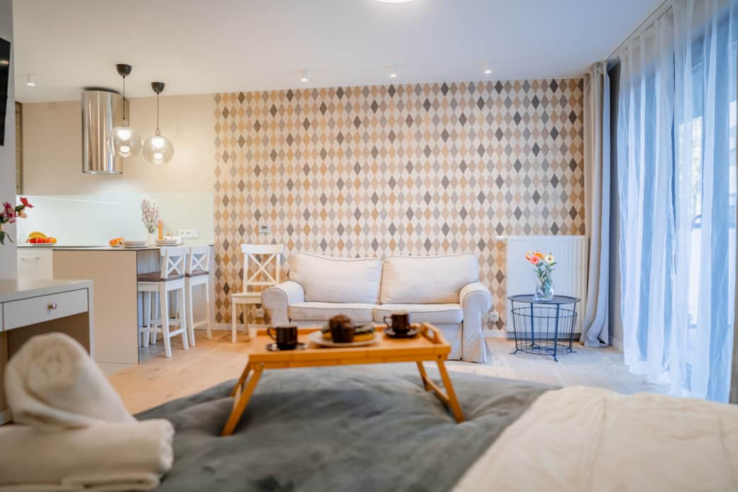 Stylowy apartament typu studio z jasną sofą, aneksem kuchennym i elegancką tapetą w geometryczny wzó