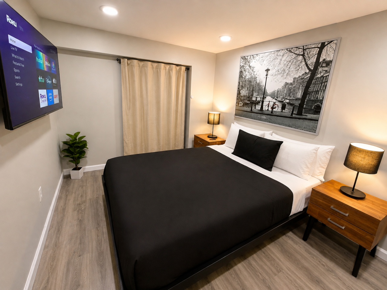 Bedroom 1: Comfortable, stylish bedroom featuring a queen-size bed, crisp bedding, warm bedside lighting, and a wall-mounted Smart TV with Roku. The room also offers a large closet with plenty of storage space, modern flooring, and relaxing décor—perfect for a comfortable stay.