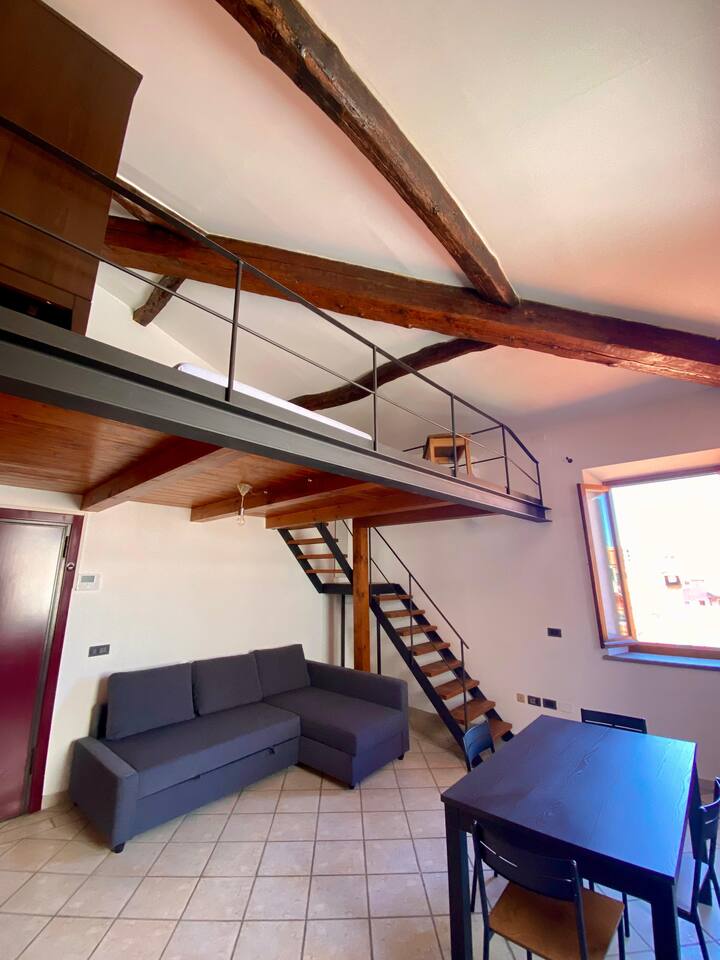 Salotto con divano letto e scale che portano alla camera con soppalco