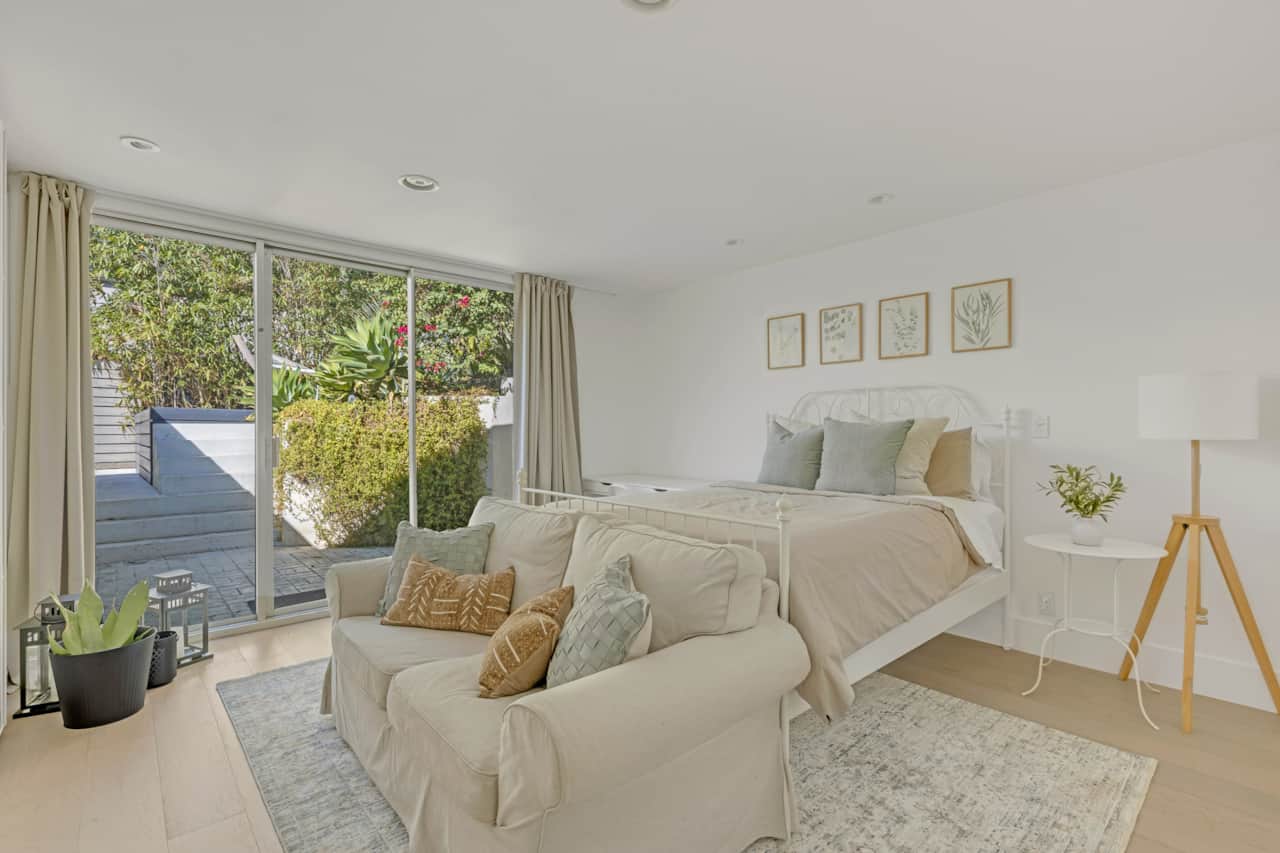 Queen bedroom with plush seating facing a neatly made bed and textured pillows.