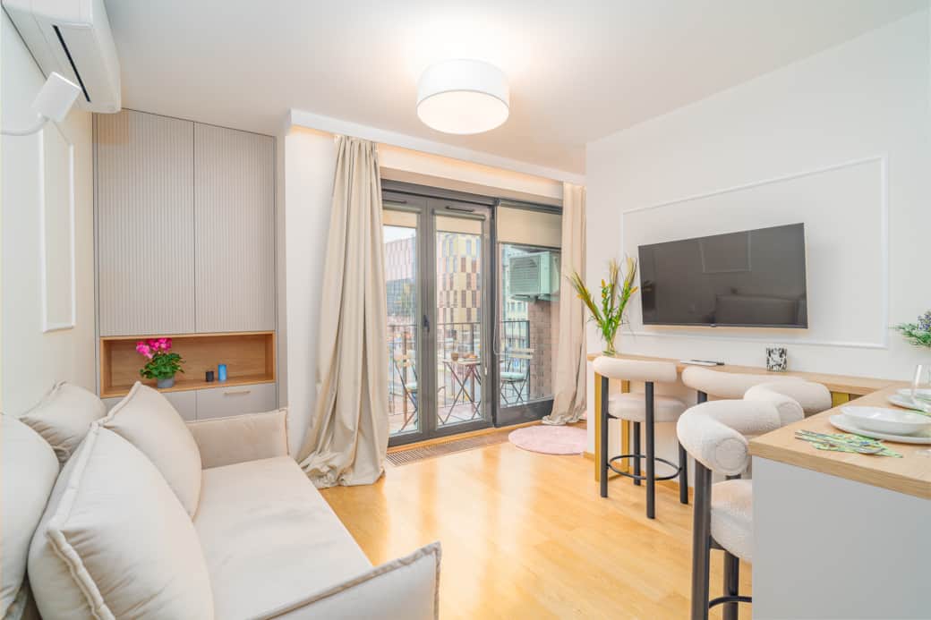 Przytulny salon z aneksem i balkonem, jasny, nowoczesny, urządzony w stonowanych barwach.