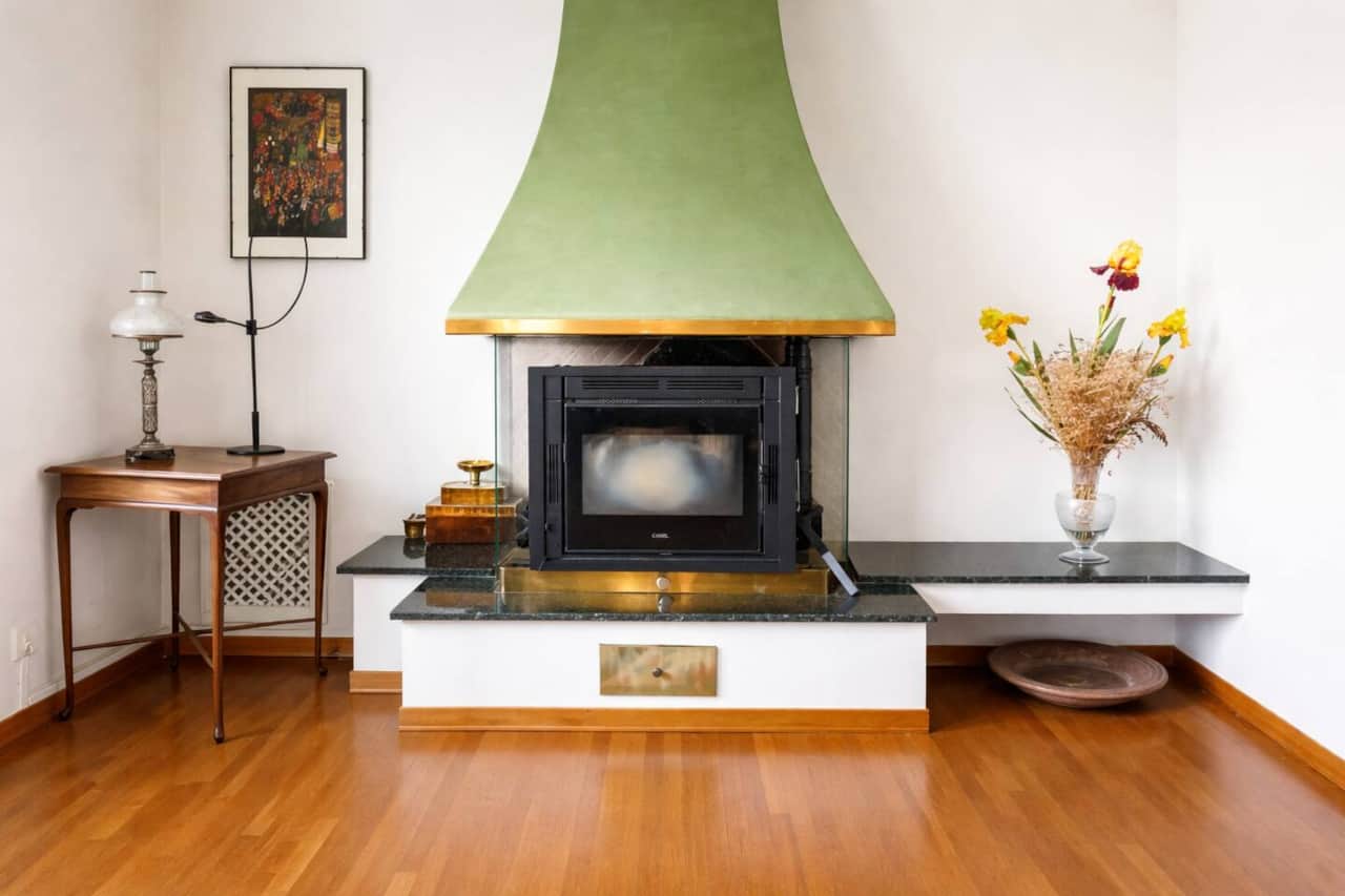 Elegante camino dal design originale con cappa verde, elemento distintivo del salotto, che dona carattere e un’atmosfera calda e accogliente all’ambiente.