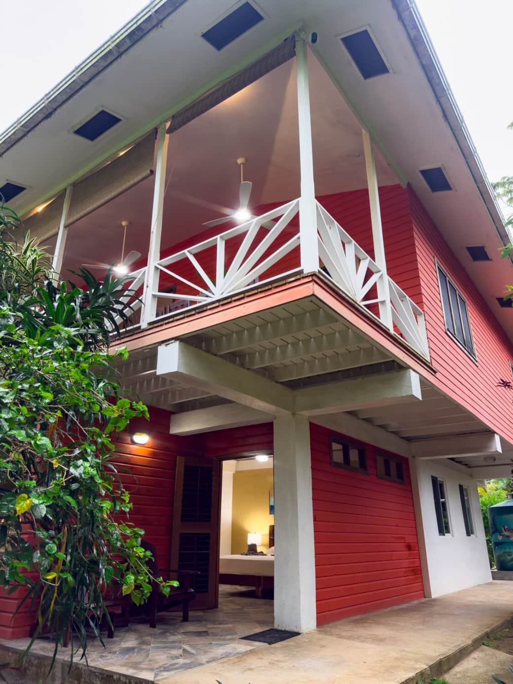 Corner exterior view of Conchy Tonk showcasing the elevated second floor, covered terrace, and garden-level entrance framed by tropical greenery.
