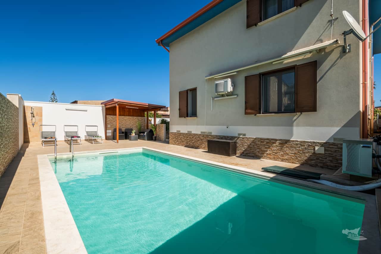 The villa boasts a heated swimming pool and a shaded lounge area with comfortable seating.