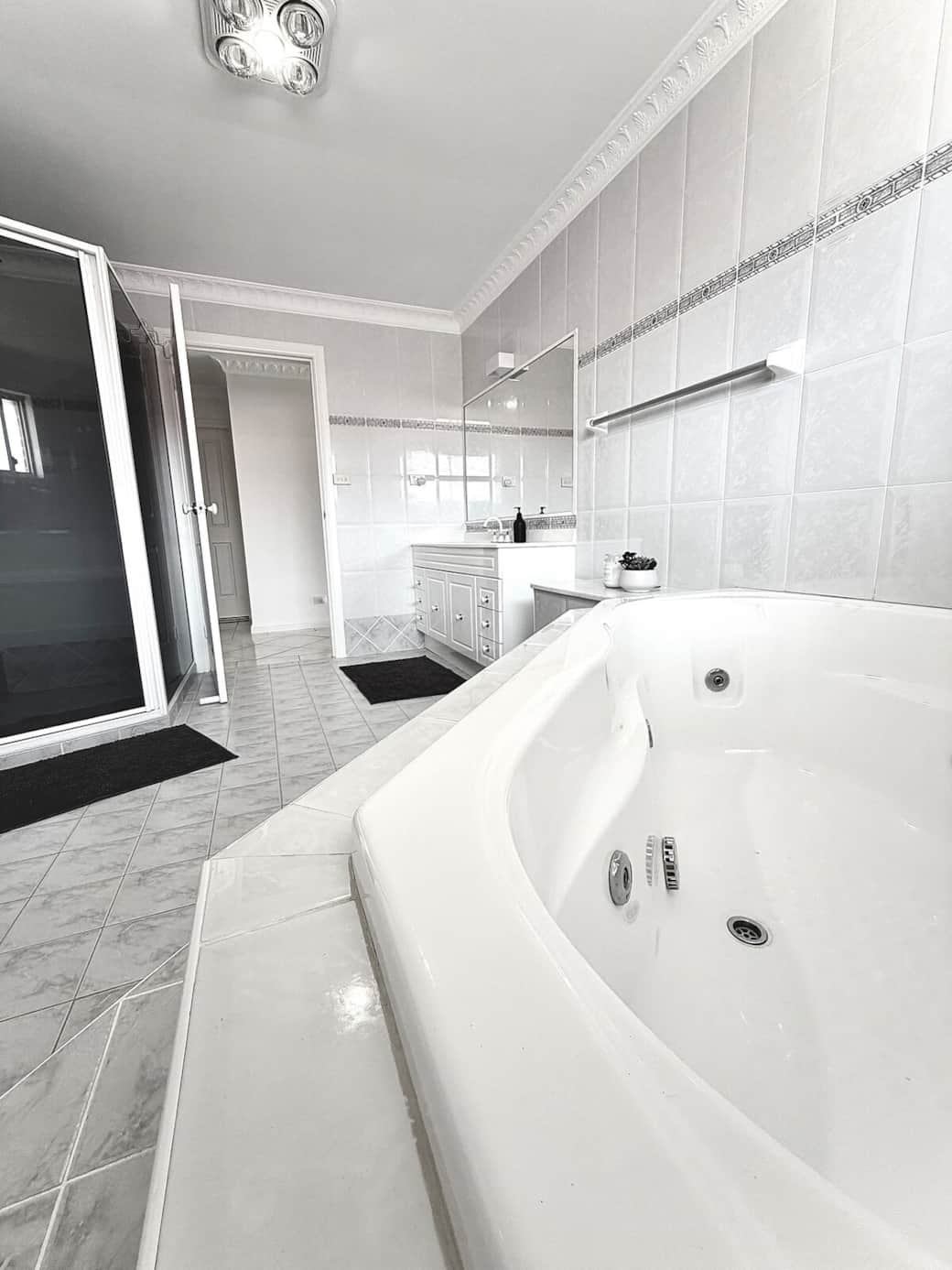 Spacious, light-filled bathroom featuring a large spa bath, separate shower, and a wide vanity. Perfect for relaxing after a day at the beach.