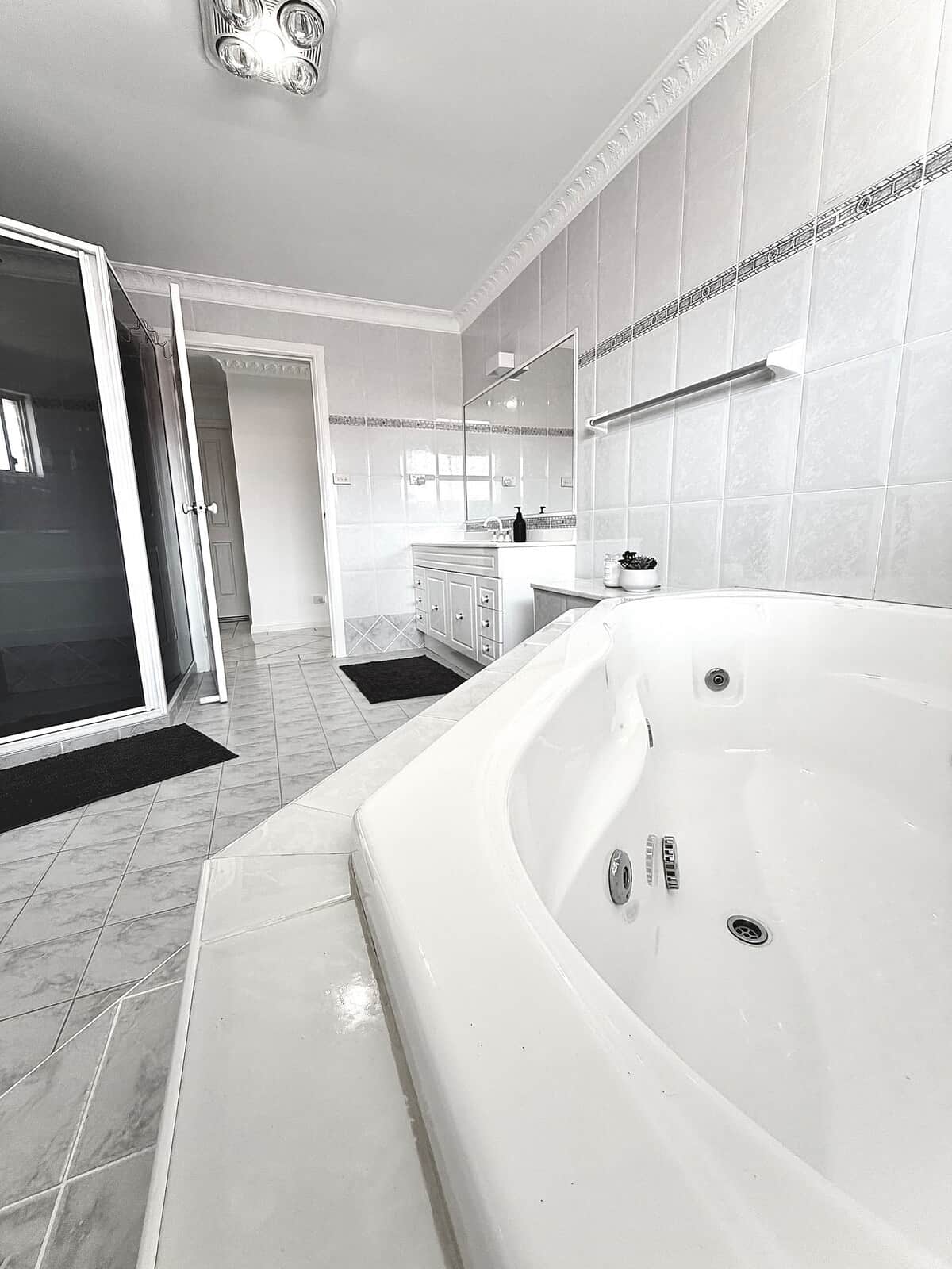 Spacious, light-filled bathroom featuring a large spa bath, separate shower, and a wide vanity. Perfect for relaxing after a day at the beach.