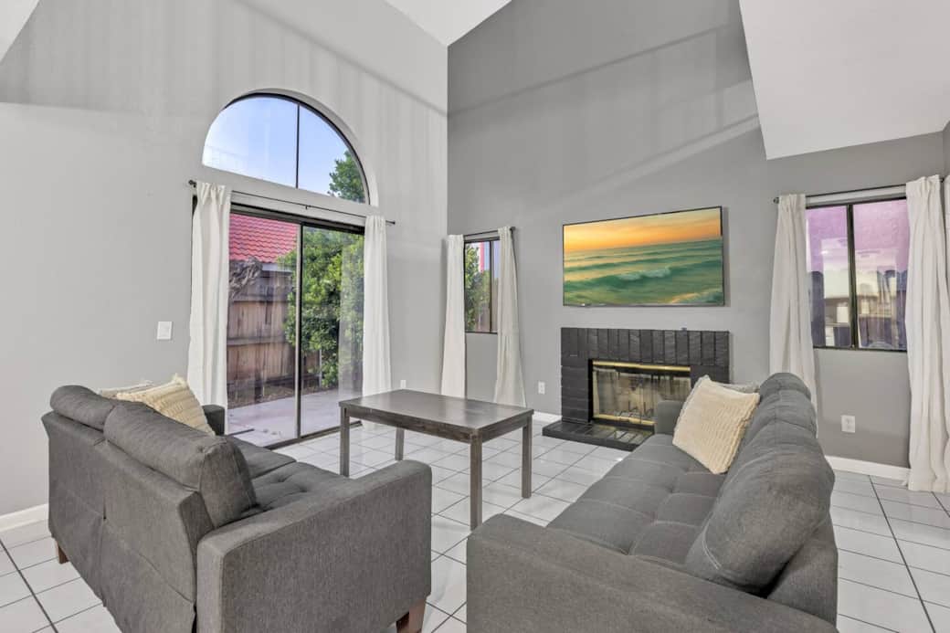 Living room area with gray sofas, fireplace, large arched window, and wall-mounted TV.