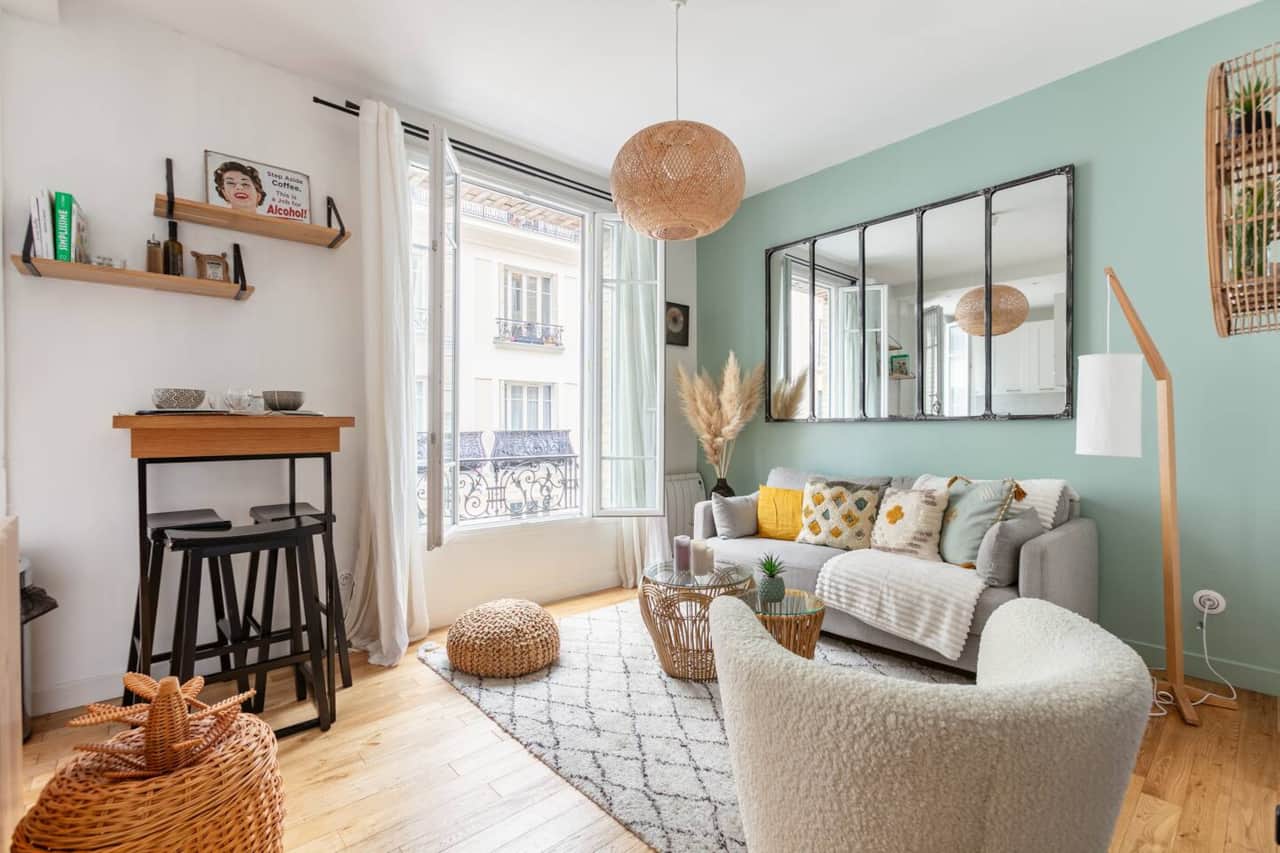 Un salon lumineux et cosy avec un canapé gris, des coussins colorés, et un miroir industriel. Une am