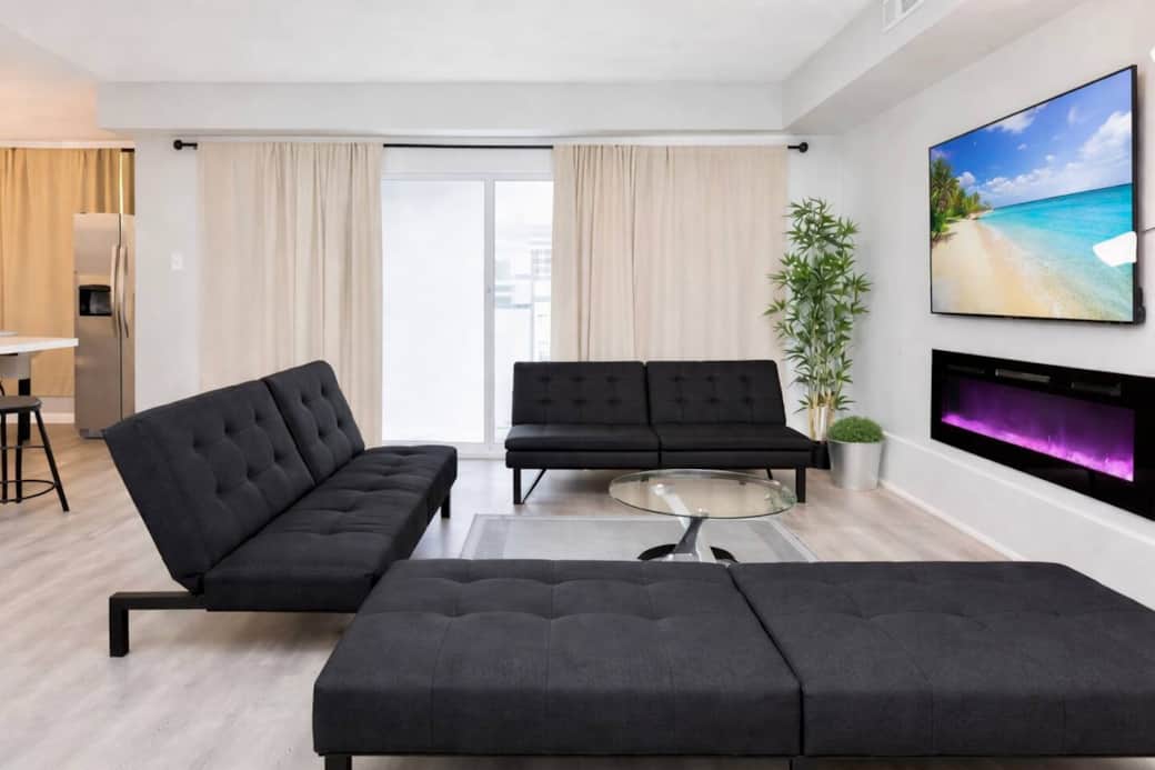 Spacious, modern living area with a 65” smart TV, three futon sofa beds, cozy fireplace, and a large balcony—perfect for relaxing. Openly connected to the kitchen and dining area for easy entertaining.