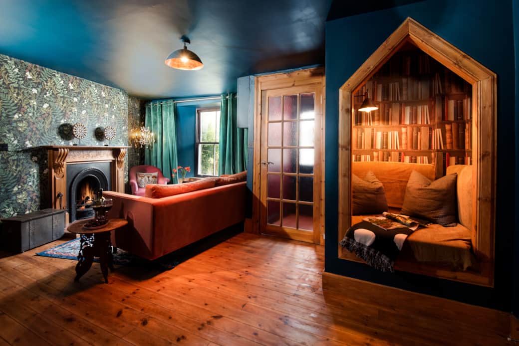 Eccentric Caterpillar lounge: Teal/blue walls, velvet sofa, fireplace, and cozy reading nook.