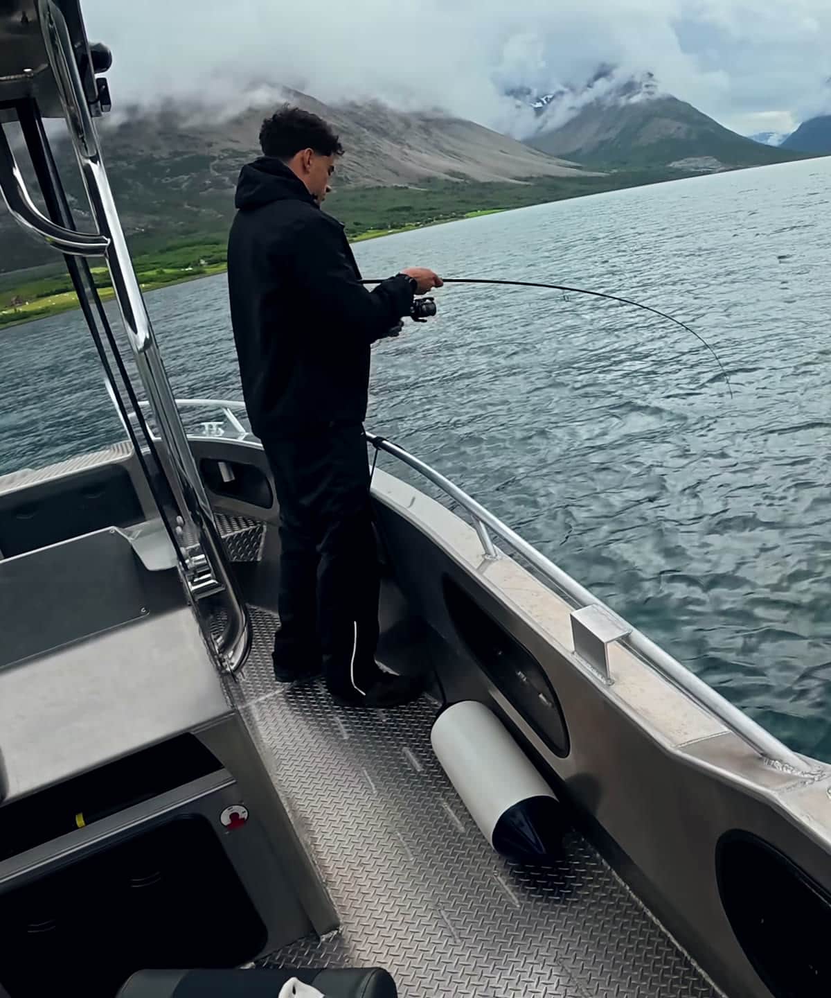 Angler am Bug des Boots, die Rute im Drill gebogen, Fjord und Berge