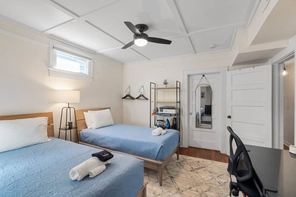 Bedroom # 2 two twin XL beds with adjoining door to bedroom #3 closed and hanging full length mirror.  Room darkening blind over the window. close hangers on the wall, large shelf with printer and random office supplies.