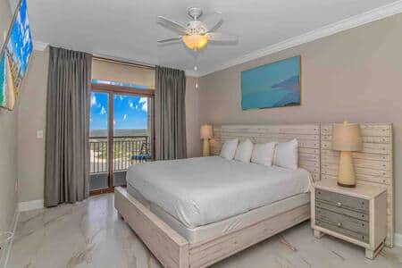 Luxurious primary suite with king bed, private balcony access, flat-screen TV, and stunning ocean vi