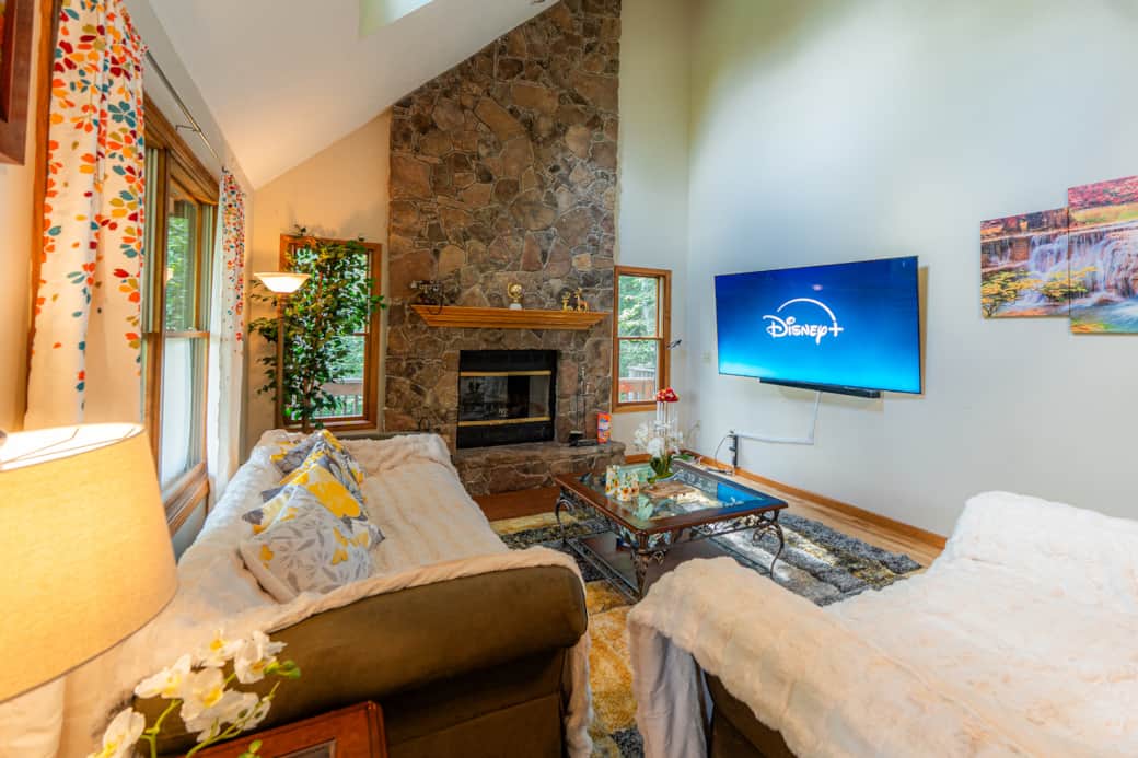 Large main living room with wood burning fireplace, dining table, and 75" smart TV