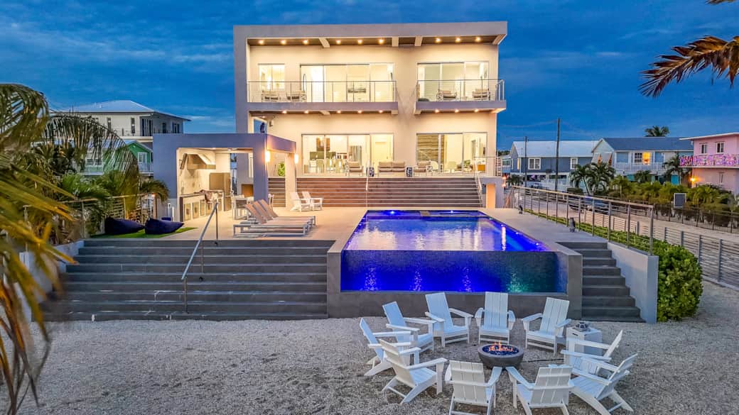 Twilight view of the home, infinity pool, lounge area and fire pit