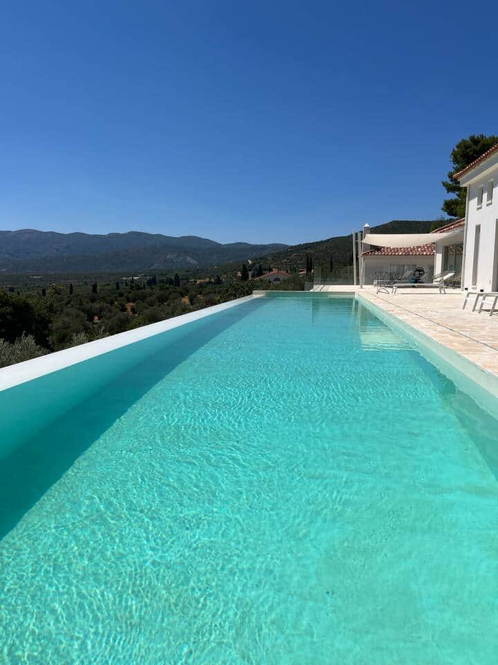 A shimmering infinity pool stretches toward rolling hills and a boundless blue sky.