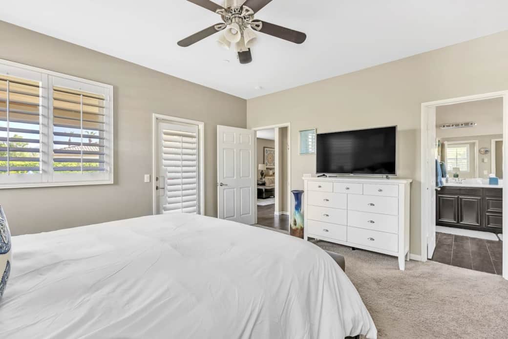 Bedroom with plush carpet, dresser, smart TV, and backyard access.