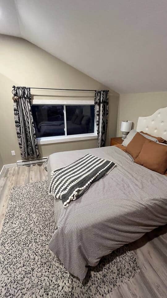 Cozy lofted bedroom with queen bed, bold drapes, and soft area rug. Cozy lofted bedroom with queen bed, bold drapes, and soft area rug.