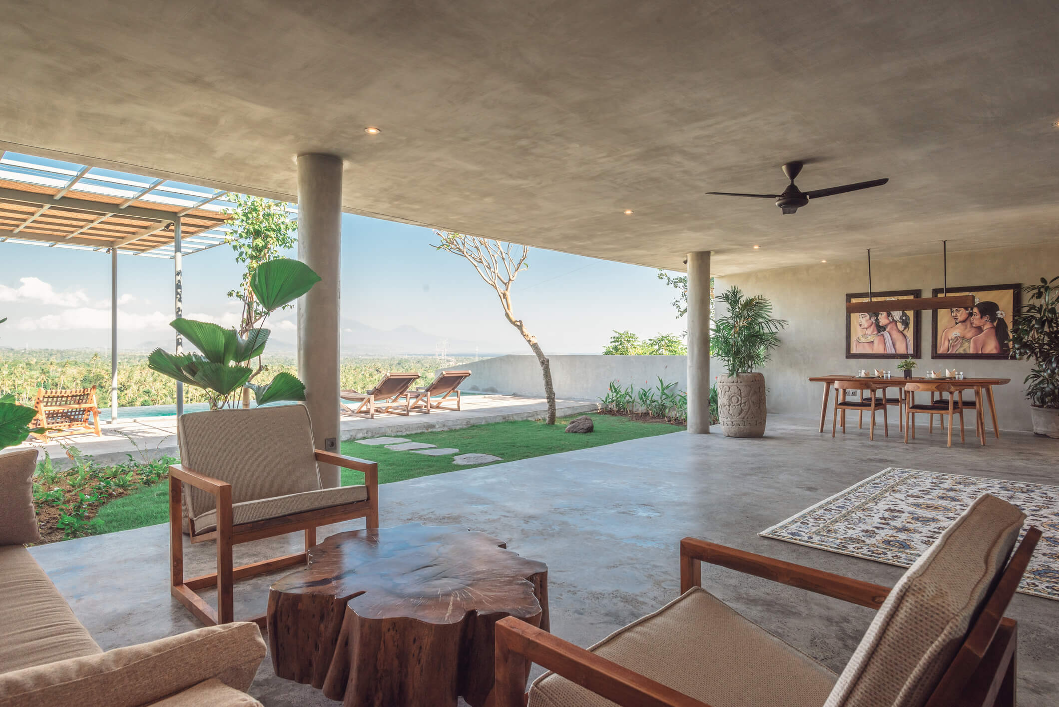 Open-plan lounge at Villa Zaphyr, Sumberkima, Bali, with wooden seating, stump coffee table and pool overlooking volcano