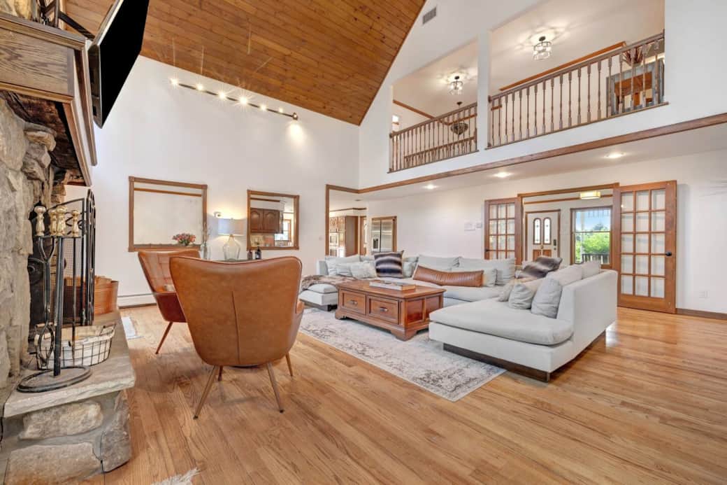 Relax in the elegant living room featuring a vaulted ceiling, grand stone fireplace, and cozy seating. Warm and inviting, it's the perfect space to unwind, connect, and enjoy the morning and evening passing of deer alongside the property.