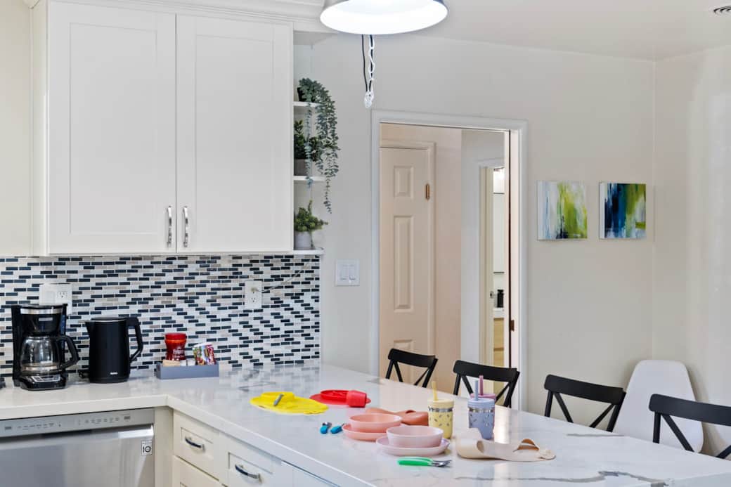 Kitchen counter with coffee maker, kettle, and colorful kids' dishes.