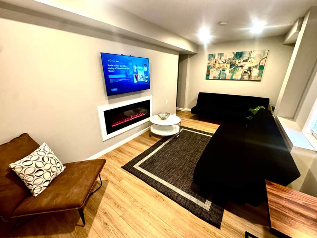 Discover our elegantly designed living room, featuring two versatile futon sofa beds, a large flat-screen television, and a cozy fireplace, providing an ideal setting for both relaxation and social gatherings.