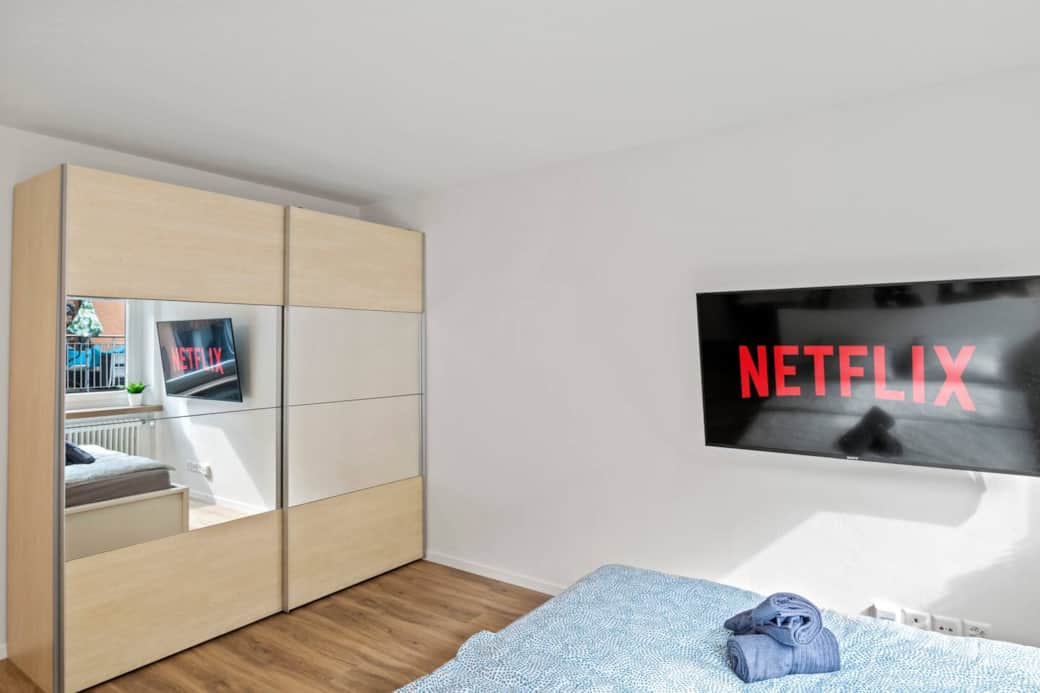 Large wardrobe with mirror right next to the bed and TV area.