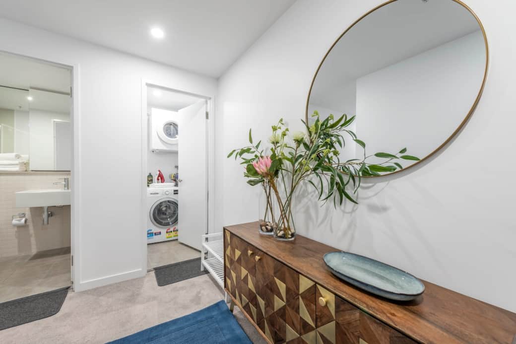 Step into our well-lit hallway, a gateway to convenience. The entrance to the bathroom and laundry area is marked by a tasteful wooden console table, adorned with a vase of fresh flowers.