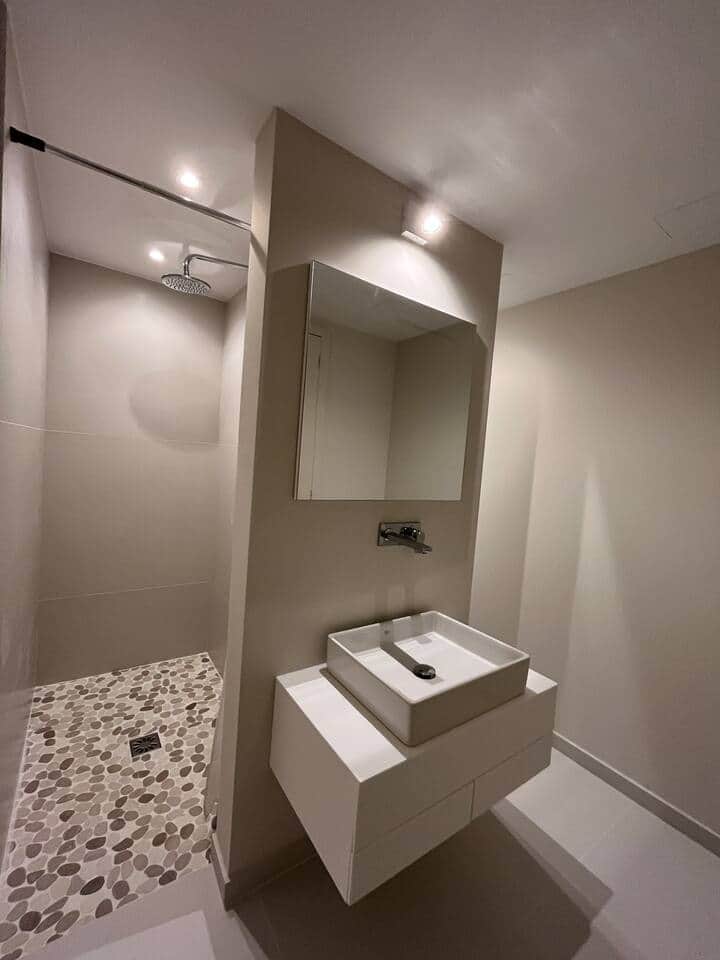 Contemporary bathroom with a central wash basin; to the left, a walk-in shower, to the right, a WC and bidet. The mirror conceals a discreet cabinet. Refined finishes and mineral, airy lines evoke the atmosphere of a contemporary spa.