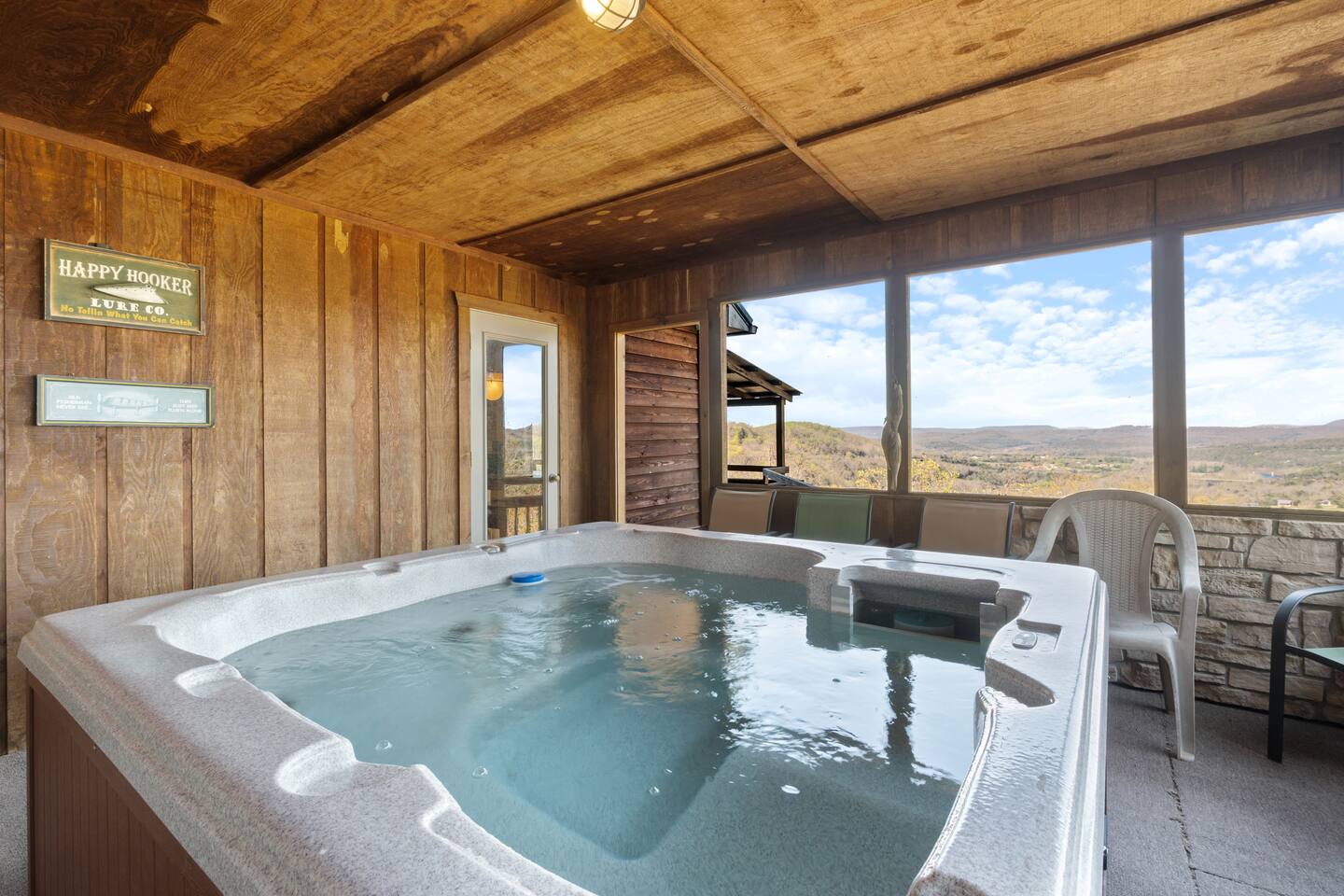 A hot tub on a wooden deck with a large window overlooking a mountain view