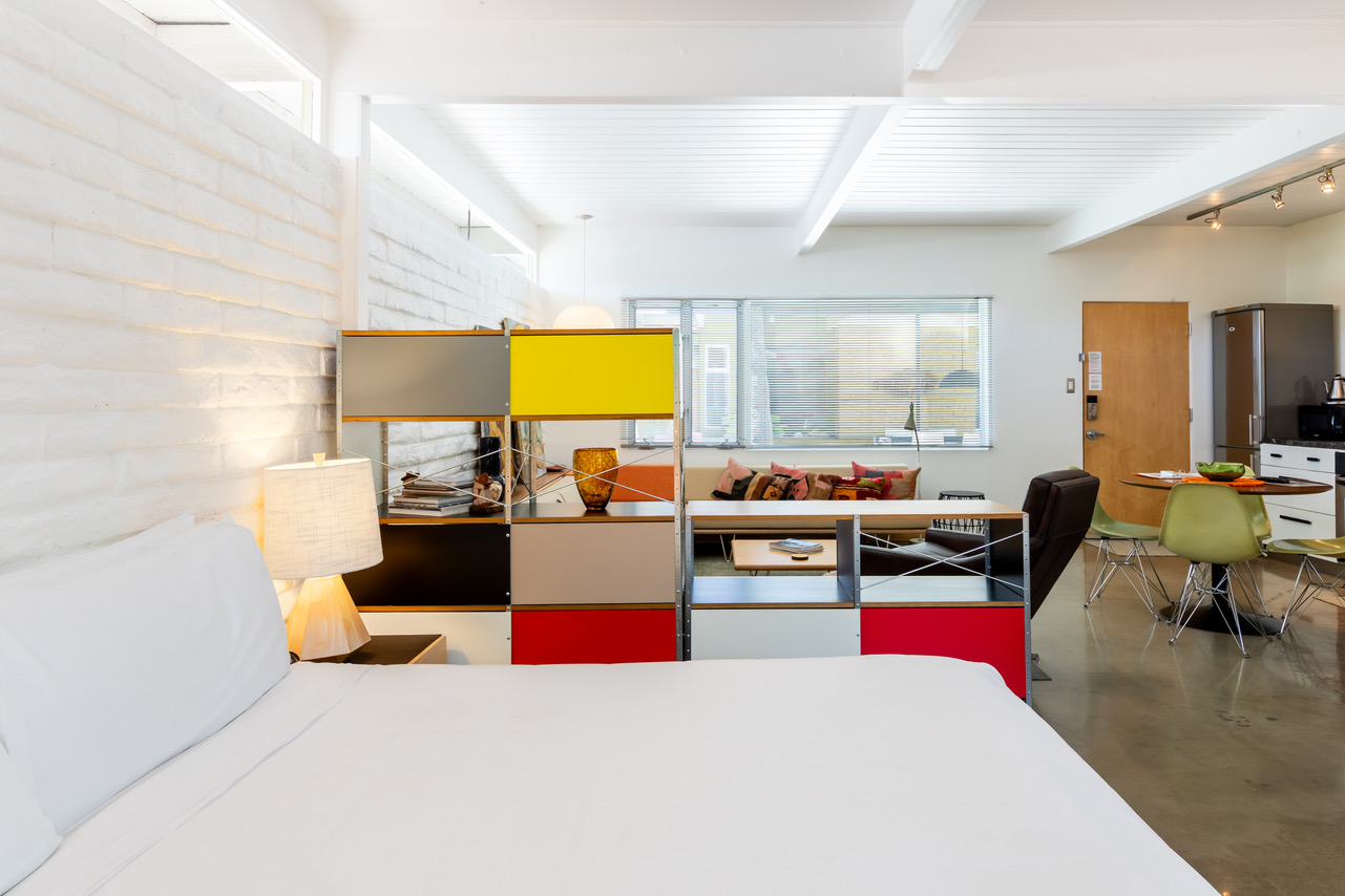 A modern suite with a king bed, sofa, desk, kitchenette, and TV