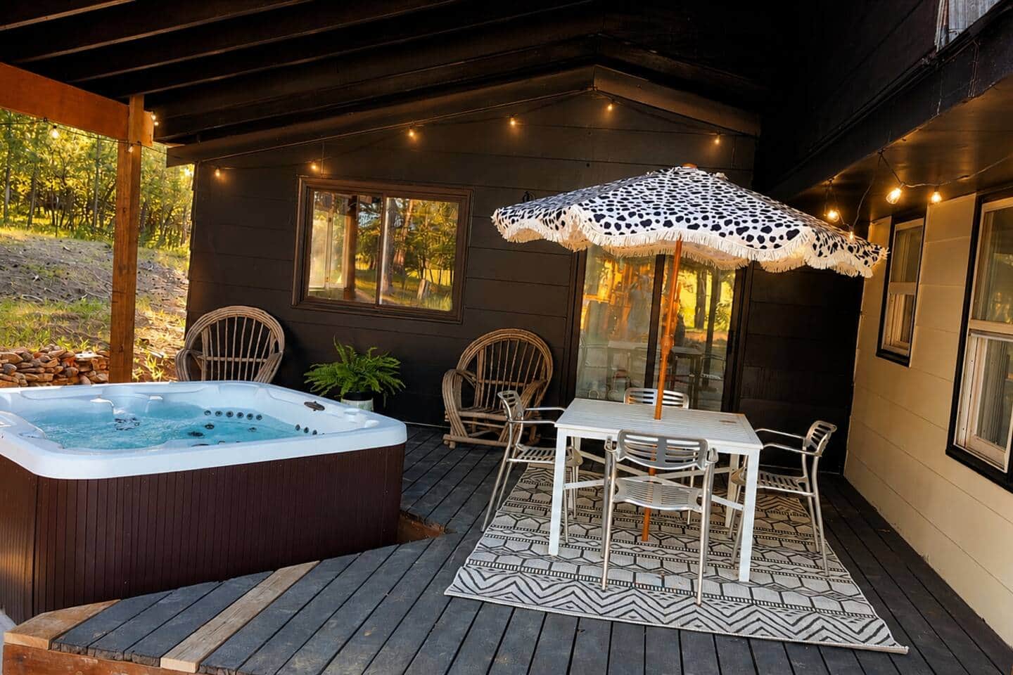 Private hot tub and outdoor dining beneath a covered deck with string lights
