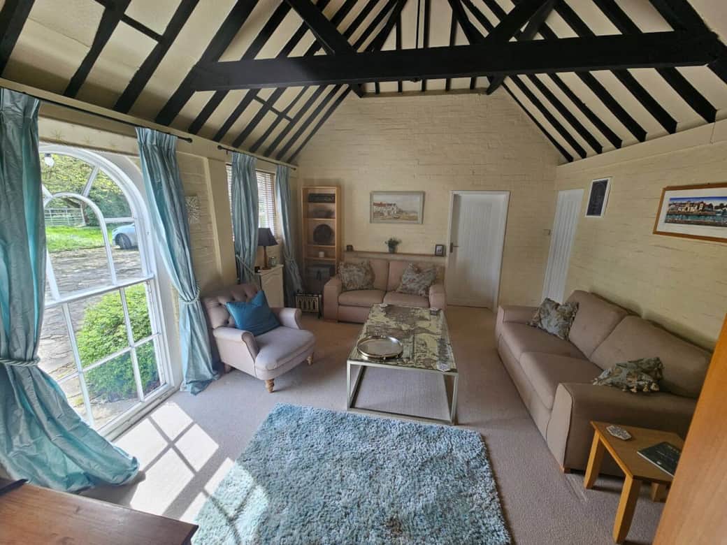 Living room with huge bright windows letting in lots of light, vaulted ceiling, comfy sofas, smart TV, bookshelves, books and games.