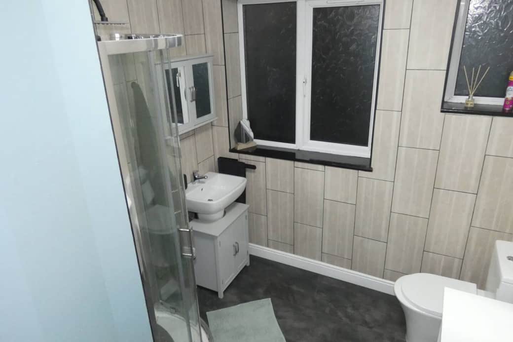 Main bathroom featuring shower cubicle with rain shower head, toilet, storage cupboards, toiletries