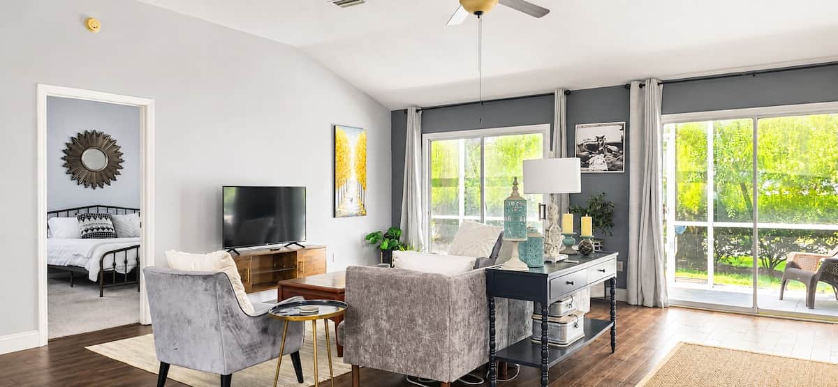 Large windows dressed in airy curtains fill the room with natural light, while the soft neutral furnishings and elegant touches create a comfortable yet polished vacation-home feel.