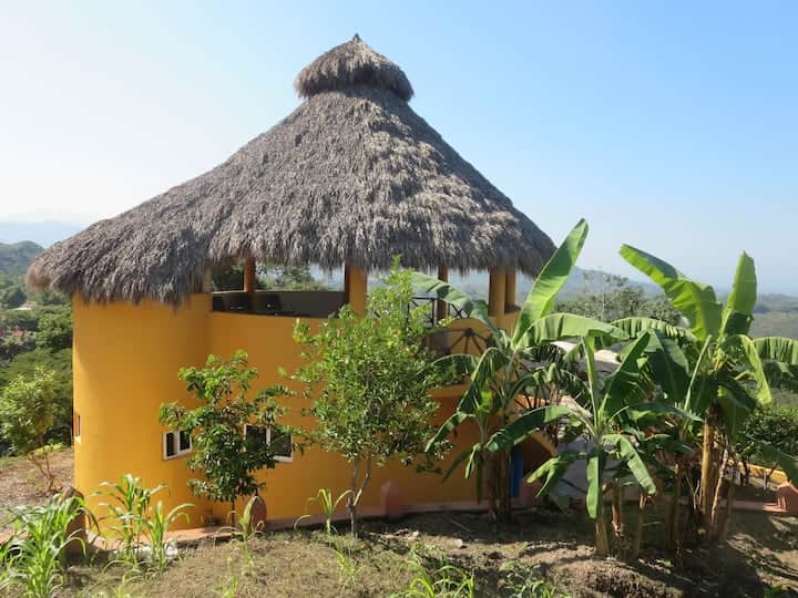 La Casa Redonda with its tall palapa roof on the hillside, surrounded by banana trees