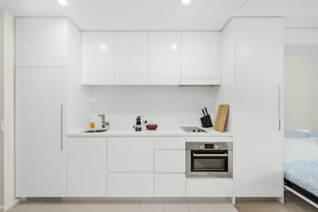 Prepare meals with ease in the sleek, fully equipped kitchen featuring modern appliances, a built-in oven, and minimalist white cabinetry. Everything you need for cooking, dining, and storing essentials is neatly arranged in this functional space.