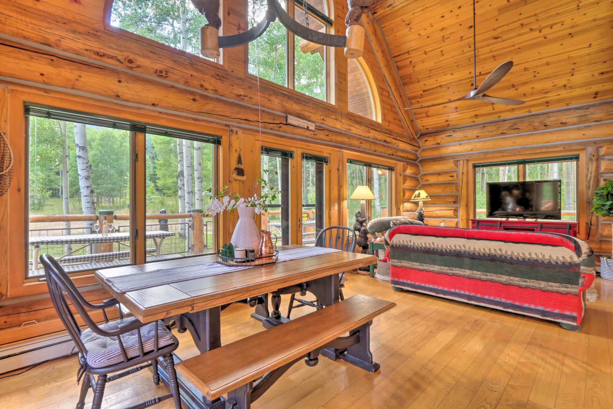 Vaulted great room with log beams and tall windows framing aspens and Spread Eagle Peak