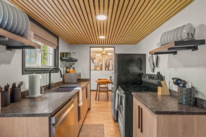 Sleek and modern kitchen with a striking wood-slat ceiling and open shelving.
